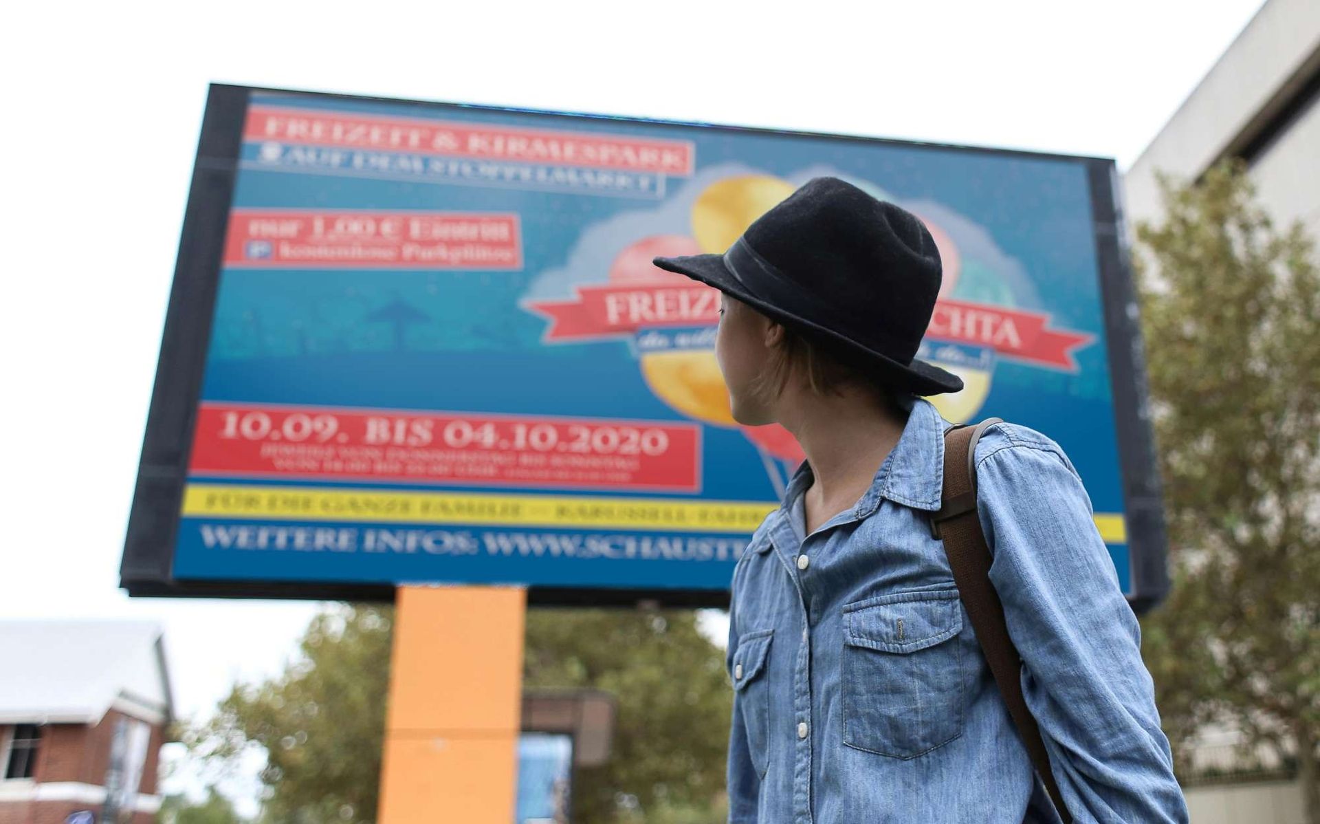 Junge Frau steht auf der Straße und schaut auf ein großes Plakat im Hintergrund